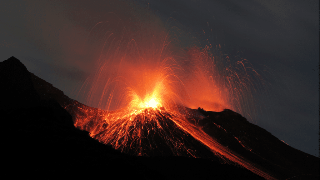 Na imagem, o vulcão Stromboli está em erupção. Ao fundo, há um céu escuro da noite.