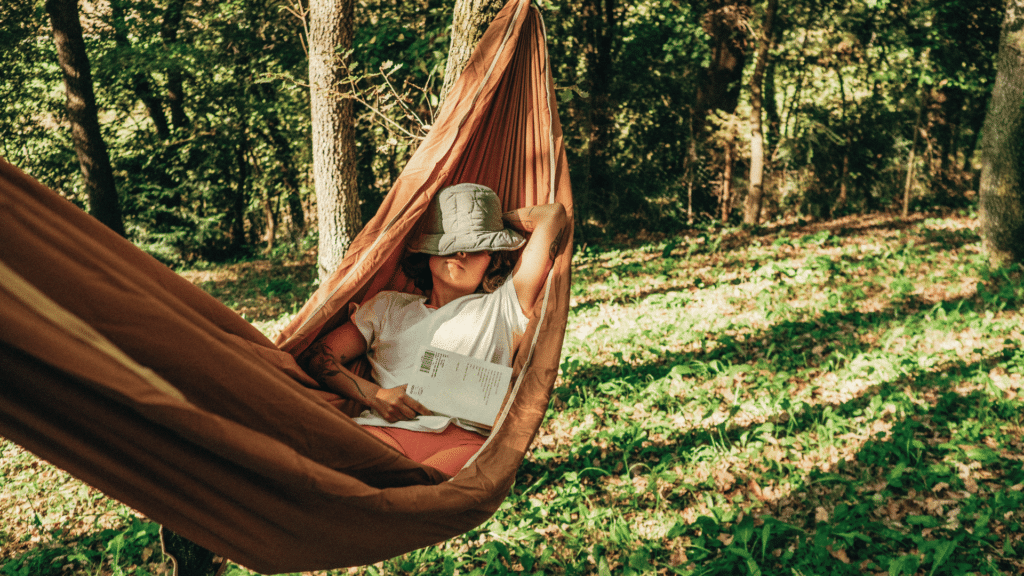 Uma mulher está deitada em uma rede. Ela está em um ambiente de natureza.