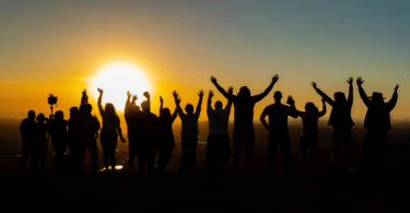 Um grupo de pessoas está contemplando o pôr do sol. Eles levantam seus braços.