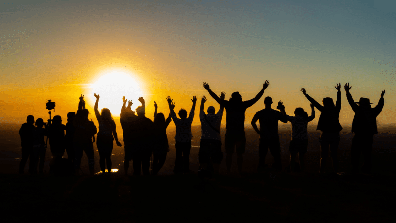 Um grupo de pessoas está contemplando o pôr do sol. Eles levantam seus braços.