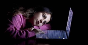 Uma mulher jovem está cabisbaixa e triste olhando e mexendo no seu notebook.