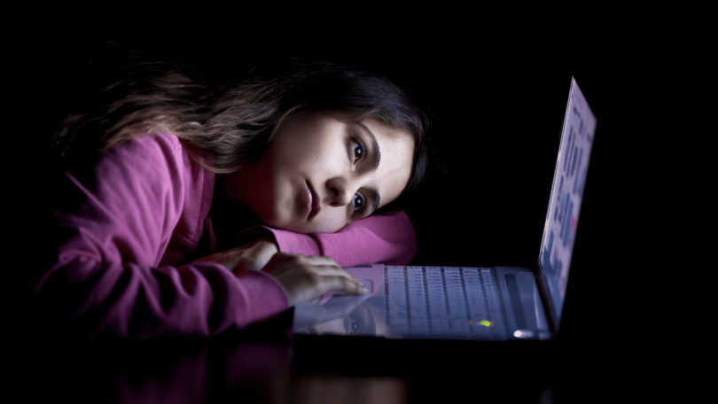Uma mulher jovem está cabisbaixa e triste olhando e mexendo no seu notebook.