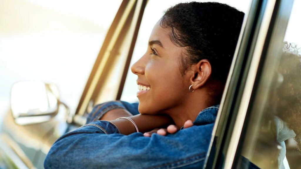Imagem de mulher preta olhando para o infinito. Ela está debruçada na janela do seu carro. A foto traz o conceito de solitude, de estar bem com você mesma.