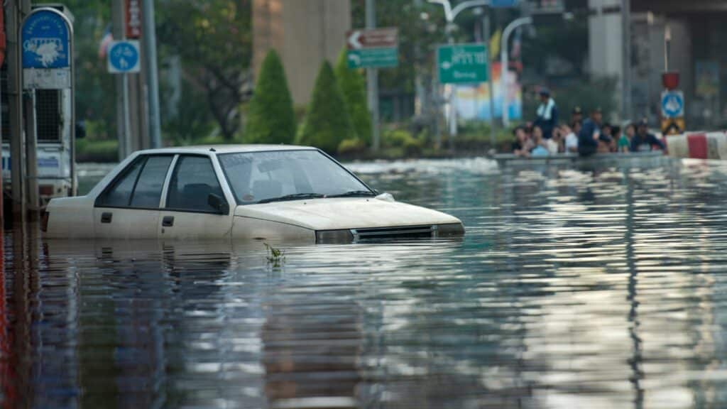 Imagem de uma rua totalmente alagada e de um carro preso na enchente.