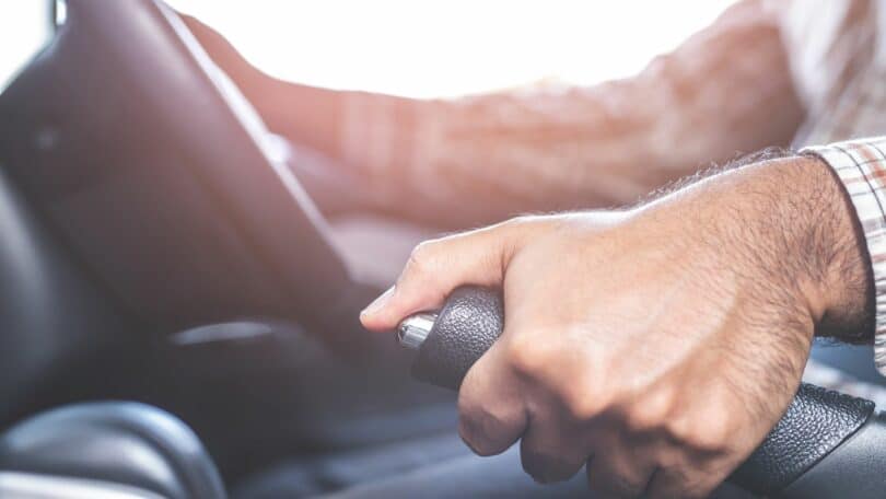 Imagem de uma mão masculina puxando o freio de mão do carro que está sem o freio de pé.