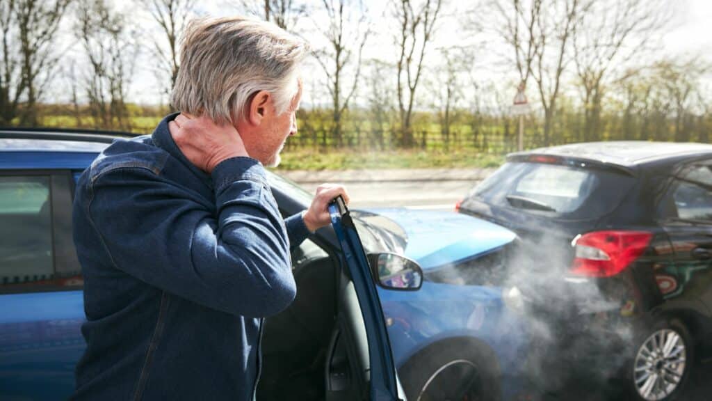 Imagem de um homem olhando o acidente que ele causou ao bater na traseira de um outro veículo porque o seu carro estava sem freio.