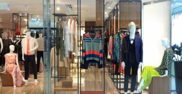 Imagem de uma loja de roupas toda feita em vidro. Destaque para os manequins espalhados por ela, usando variados estilos.