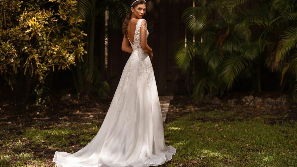 Imagem de uma noiva com o seu vestido longo branco, posando para foto em um jardim.
