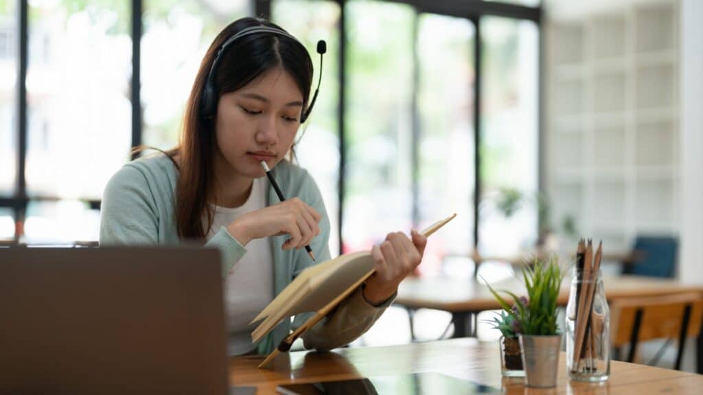 Imagem de uma mulher asiática lendo e estudando o seu livro. A foto traz o conceito da mulher que fala sobre tudo, quer entender tudo, busca cursos, livros, respostas, rituais… mas não vive. Está tão ocupada tentando interpretar o sagrado que não o integra.