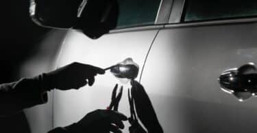 Imagem em preto e branco e em destaque as mãos de um assaltante tentando abrir a porta de um carro.