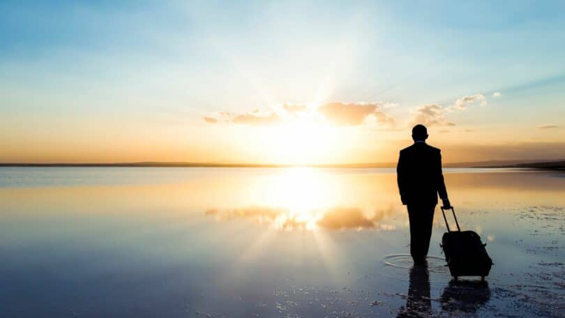 Imagem de um lindo rio e ao fundo, o pôr do sol. Em destaque, um homem puxando a sua mala. A foto traz o conceito de que a vida é uma viagem.