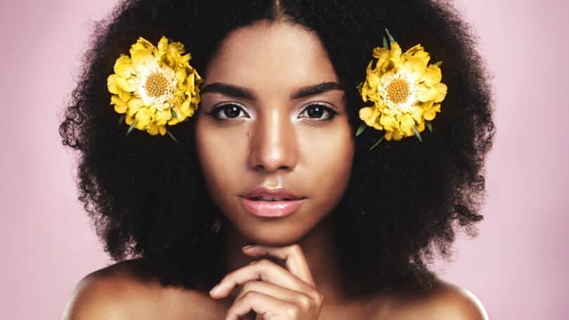 Imagem de uma linda mulher preta com seus cabelos naturais decorados com duas flores amarelas, uma de cada lado. A foto traz o conceito de autenticidade, de ser autêntico.