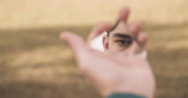O olhar de um homem está sendo refletido em um pedaço de espelho quebrado, o qual ele está segurando.