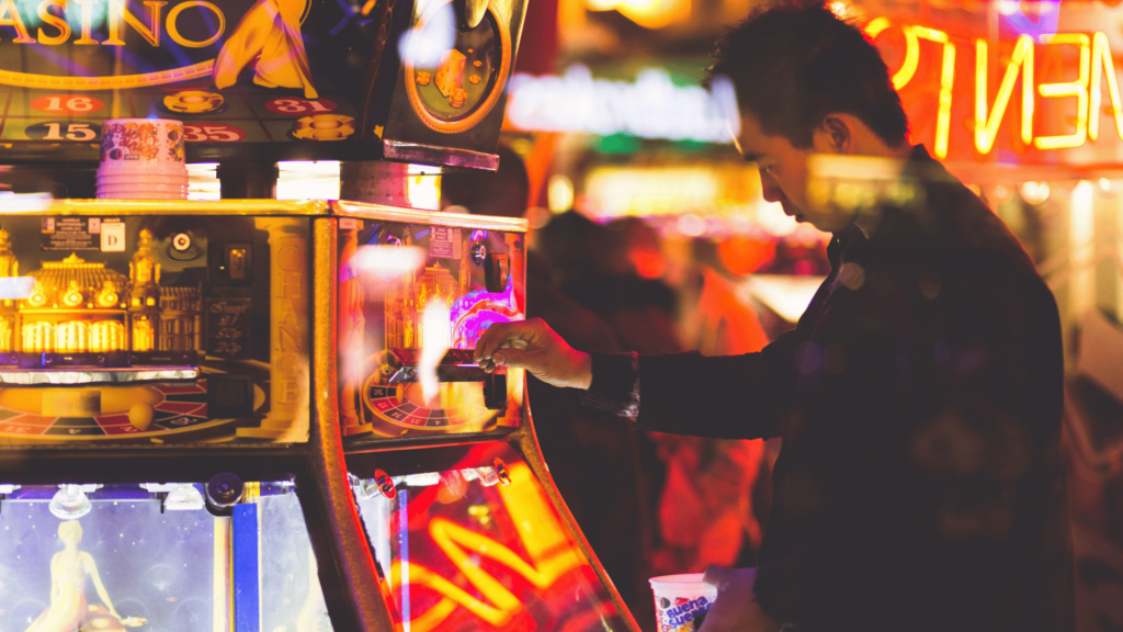Um homem está jogando em uma máquina de caça-níquel. Há luzes neon por todos os lados.