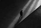 Um homem está caminhando solitário em uma cidade. A foto está em preto e branco.