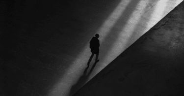 Um homem está caminhando solitário em uma cidade. A foto está em preto e branco.