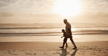 Um avô e seu neto estão caminhando na praia sob a luz do pôr do sol.