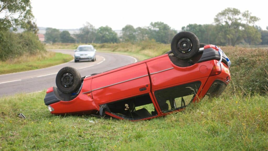 Imagem de um carro vermelho capotado em um lado da pista. O carro está sobre um gramado.