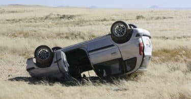 Imagem de um carro cinza capotado em um campo.