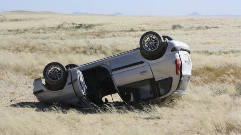 Imagem de um carro cinza capotado em um campo.
