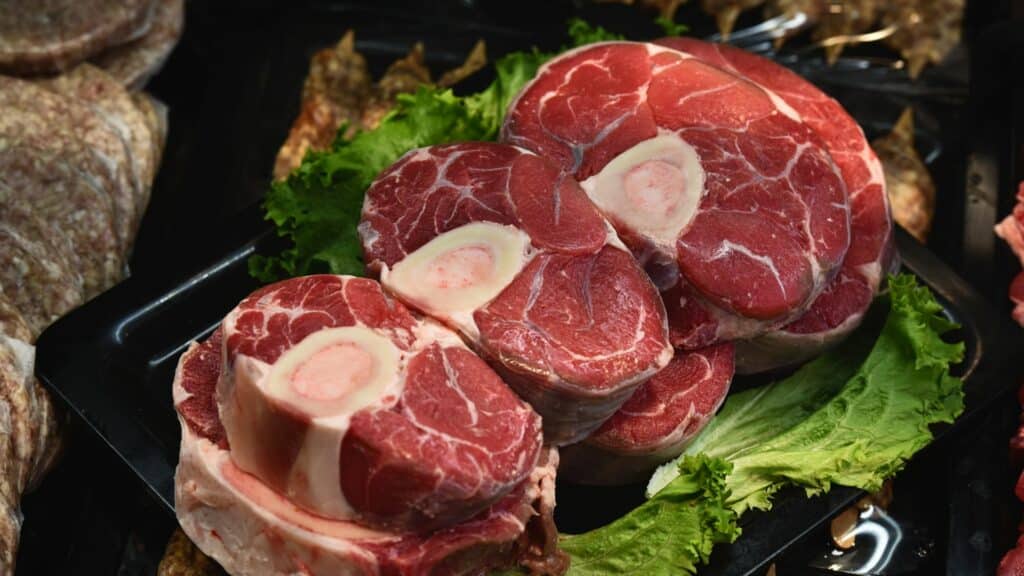 Imagem de vários pedaços de carne crua vermelha dispostos sobre folhas de alface em uma grelha.