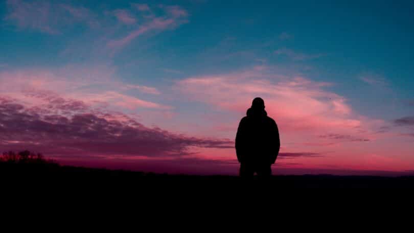 Imagem de um lindo pôr do sol meio rosado e em destaque a silhueta de um homem.