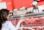 Imagem de uma mulher comprando carne de boi em um açougue. Ela está sendo atendida por um açougueiro.