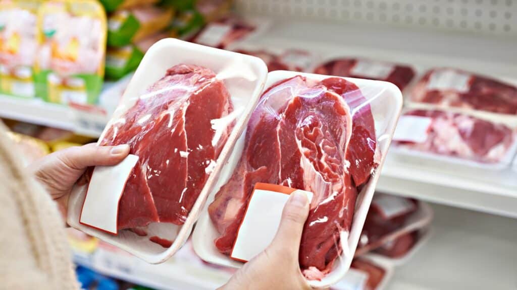 Imagem das mãos de uma mulher segurando duas bandejas de carne de boi. Ela está escolhendo qual comprar.
