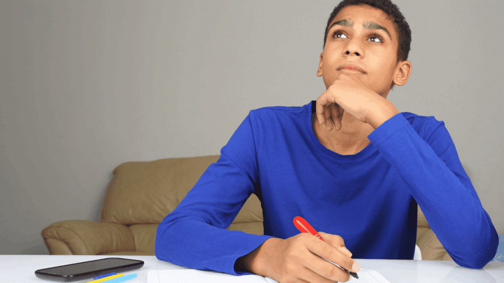 Um adolescente está estudando. Ele coloca a mão no queixo e olha para cima, indicando que está refletindo sobre algo.