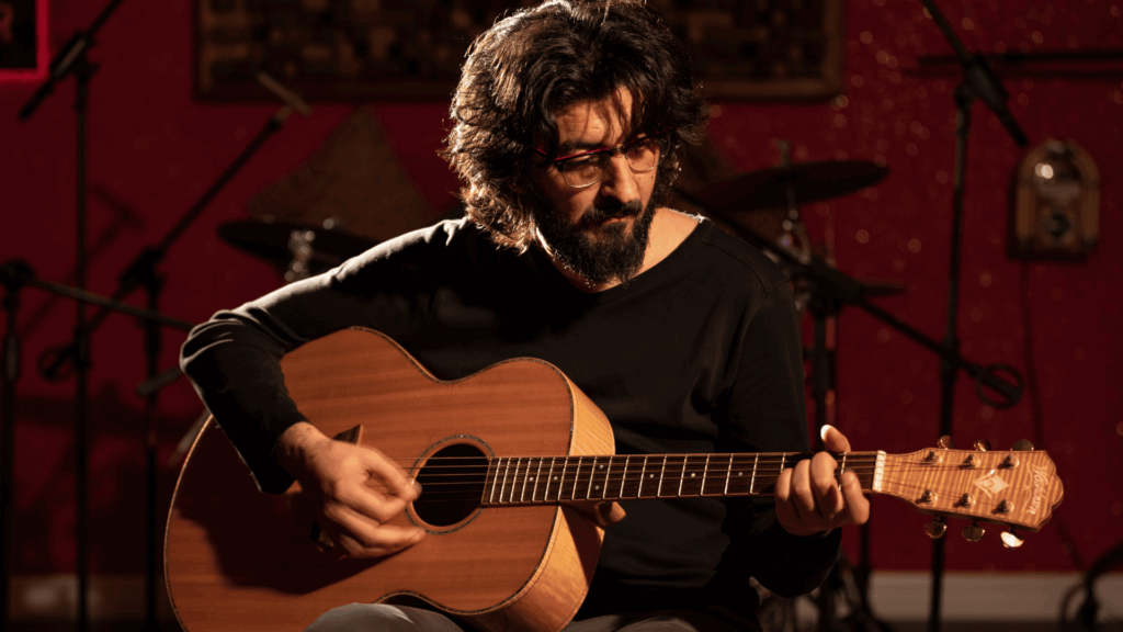 Um homem e artista tocando violão está no foco da imagem.