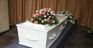 Imagem de um caixão branco de um bebê que faleceu. Sobre ele, uma coroa de rosas.