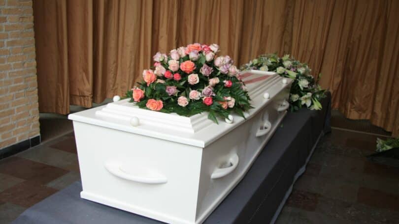 Imagem de um caixão branco de um bebê que faleceu. Sobre ele, uma coroa de rosas.