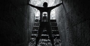 Imagem de um homem dentro de um túnel feito de pedras. Ela segura com as mãos as paredes. A foto traz o conceito de resistência e força interior.