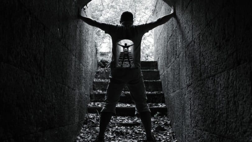 Imagem de um homem dentro de um túnel feito de pedras. Ela segura com as mãos as paredes. A foto traz o conceito de resistência e força interior.