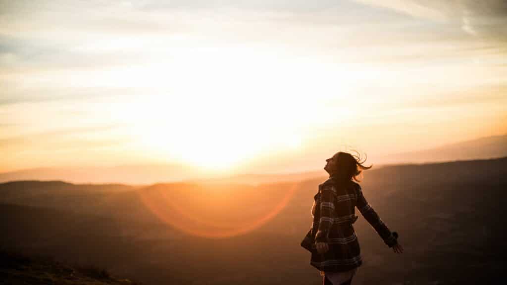 Imagem de uma mulher em um campo, olhando para o pôr do Sol. A foto traz o conceito de resistência, coragem e busca interior que nos permite enfrentar desafios, superar obstáculos e persistir mesmo diante de dificuldades.