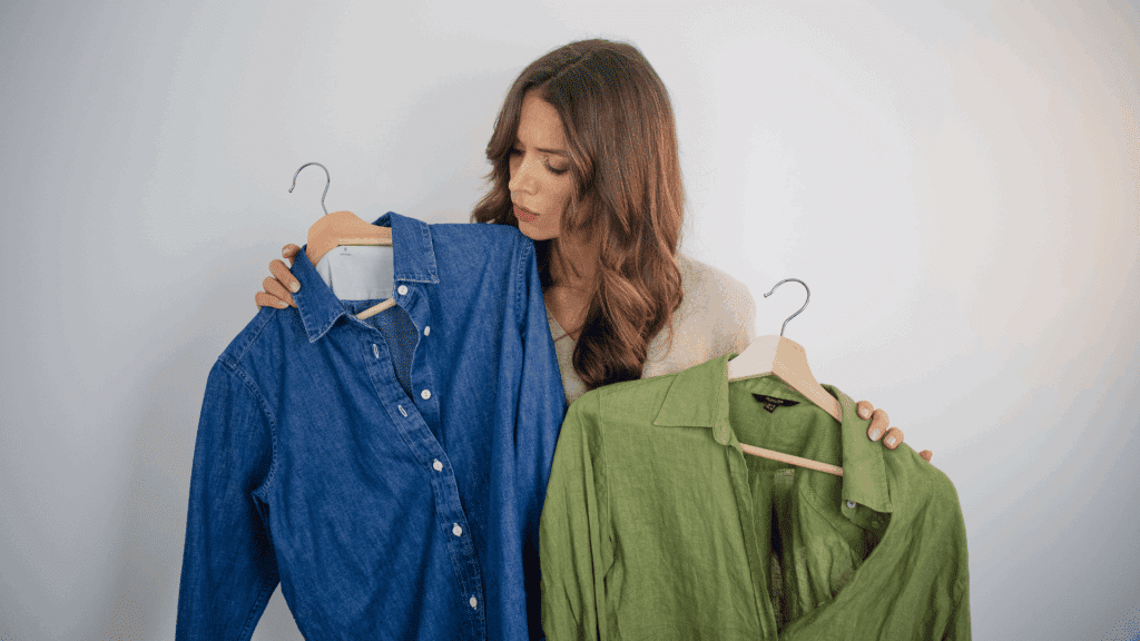 Na imagem, uma mulher está em dúvida entre duas camisas: uma azul e outra verde.