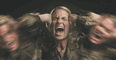 Mulher em uniforme camuflado gritando com as mãos na cabeça, transmitindo estresse e angústia.