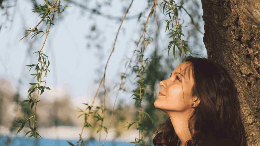 No foco da imagem, há uma mulher observando a natureza e uma árvore ao redor.