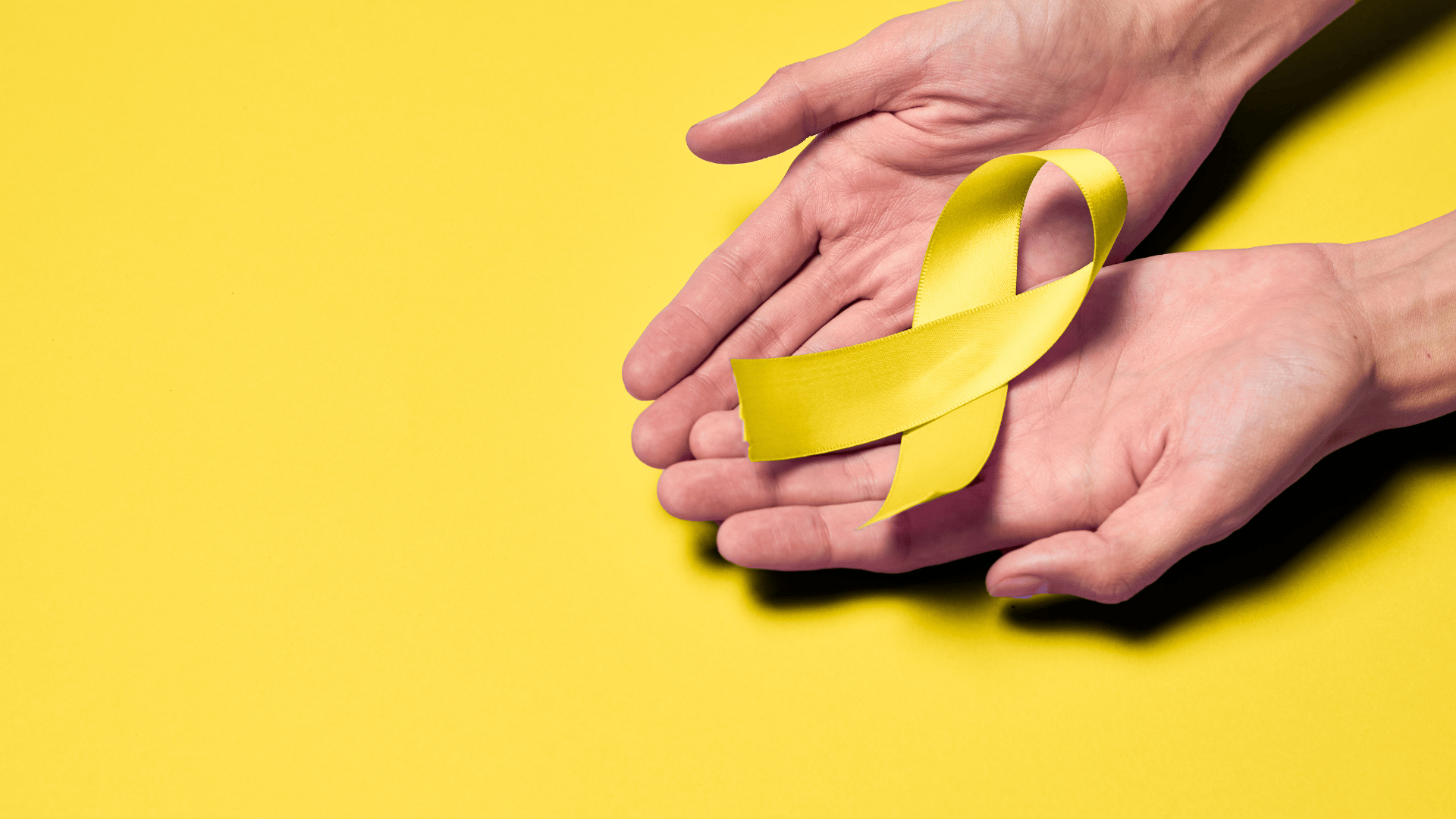 Na imagem, há as mãos de uma pessoa segurando o laço amarelo que representa o Setembro Amarelo (Dia Mundial de Prevenção ao Suicídio).