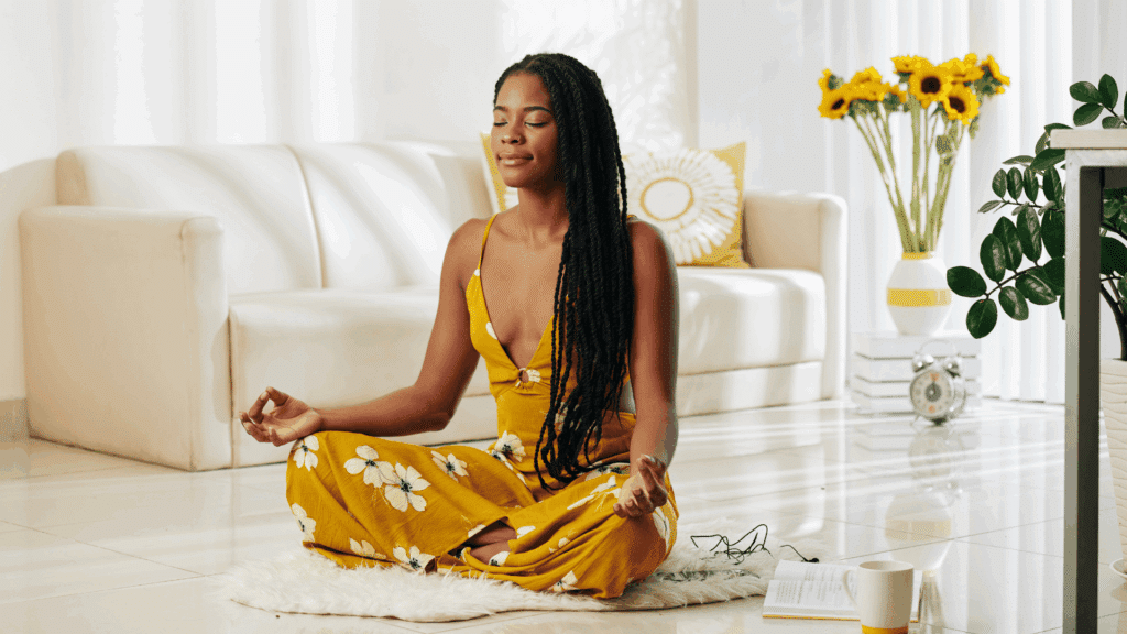 Mulher meditando em posição de lótus dentro de uma sala iluminada, transmitindo calma e bem-estar.