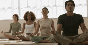 Grupo de pessoas meditando em posição de lótus, com olhos fechados e expressão serena.
