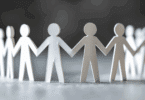 Na imagem, há papéis cortados no formato de indivíduos, os quais formam um círculo e seguram as mãos, indicando suporte, apoio, união.