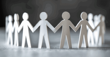 Na imagem, há papéis cortados no formato de indivíduos, os quais formam um círculo e seguram as mãos, indicando suporte, apoio, união.