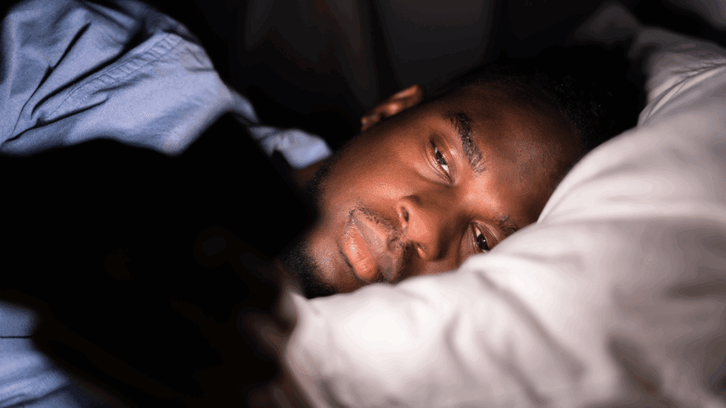 Na imagem, há um homem deitado na cama e mexendo no celular antes de dormir.