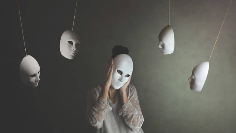 Imagem de uma mulher colocando um máscara sobre o rosto. Várias outras máscaras compõem a imagem, ficando penduradas, simbolizando o velho ditado que diz: o que as pessoas dizem sobre você revela mais sobre elas do que sobre você.