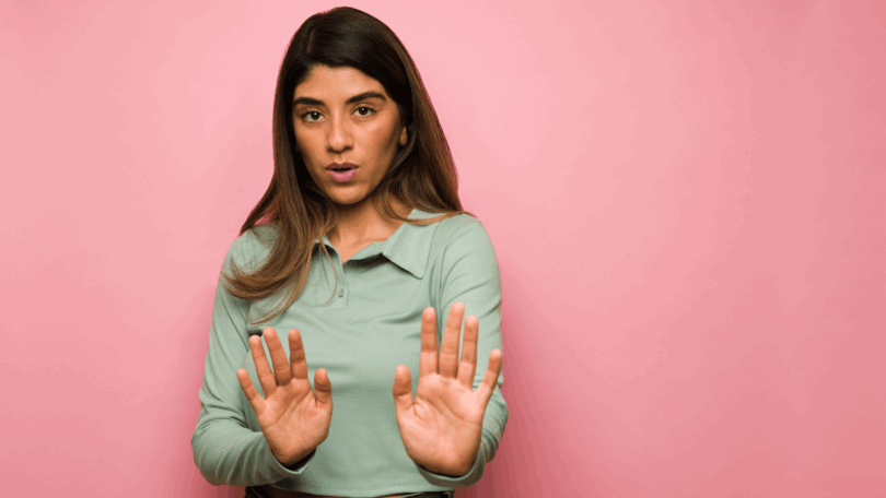Na imagem, há uma mulher que está com a expressão de medo. Ela coloca a duas mãos para frente do corpo como se pedisse espaço pessoal.