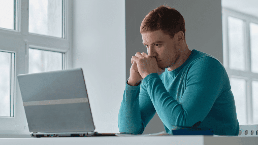 Um homem está usando o seu notebook. Ele olha para o objeto como se estivesse esperando-o carregar ou funcionar.