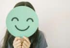 Menina pré-adolescente segurando um sorriso verde e feliz cobrindo o rosto, avaliação de saúde mental, bem-estar positivo infantil, conceito do Dia Mundial da Saúde Mental.