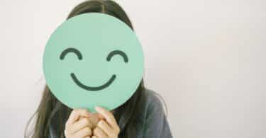 Menina pré-adolescente segurando um sorriso verde e feliz cobrindo o rosto, avaliação de saúde mental, bem-estar positivo infantil, conceito do Dia Mundial da Saúde Mental.