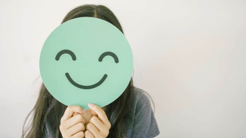 Menina pré-adolescente segurando um sorriso verde e feliz cobrindo o rosto, avaliação de saúde mental, bem-estar positivo infantil, conceito do Dia Mundial da Saúde Mental.